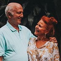 An older, white man and woman, facing each other and laughing.